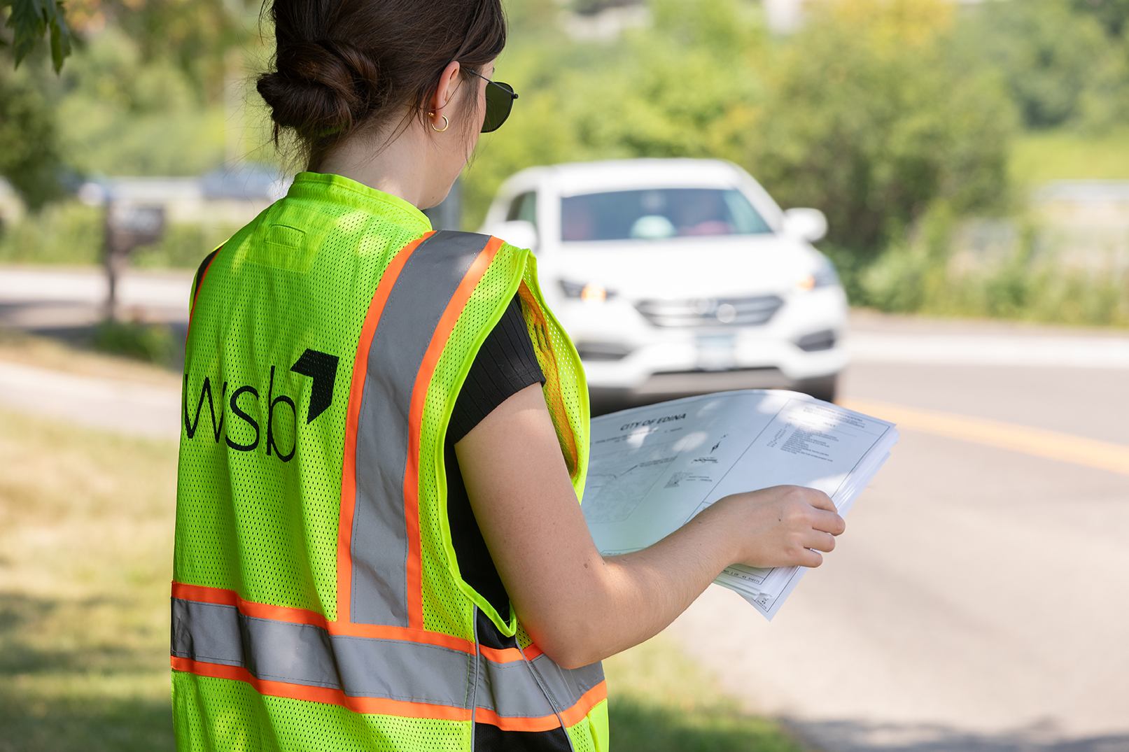 Woman wearing visibility vest review traffic plans on the side of a road