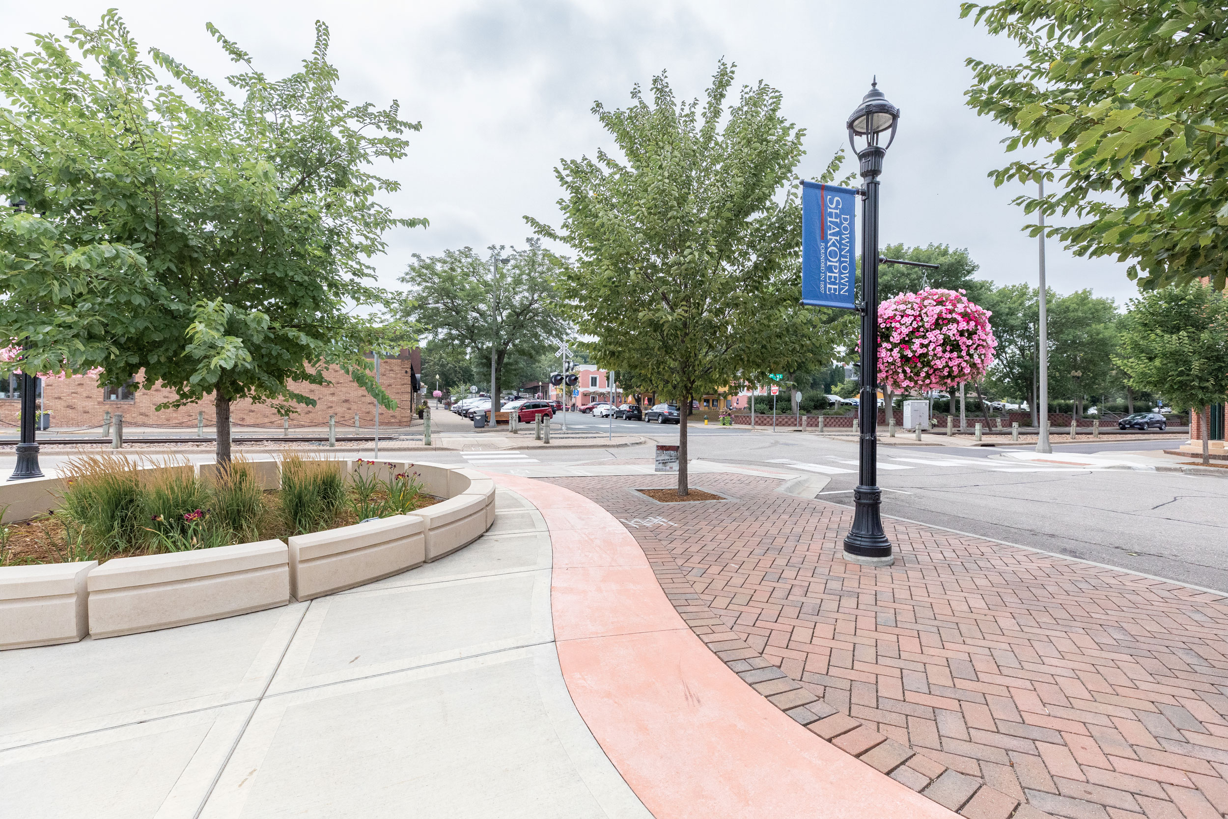 A concrete and bricked pathway with grennery next to a road