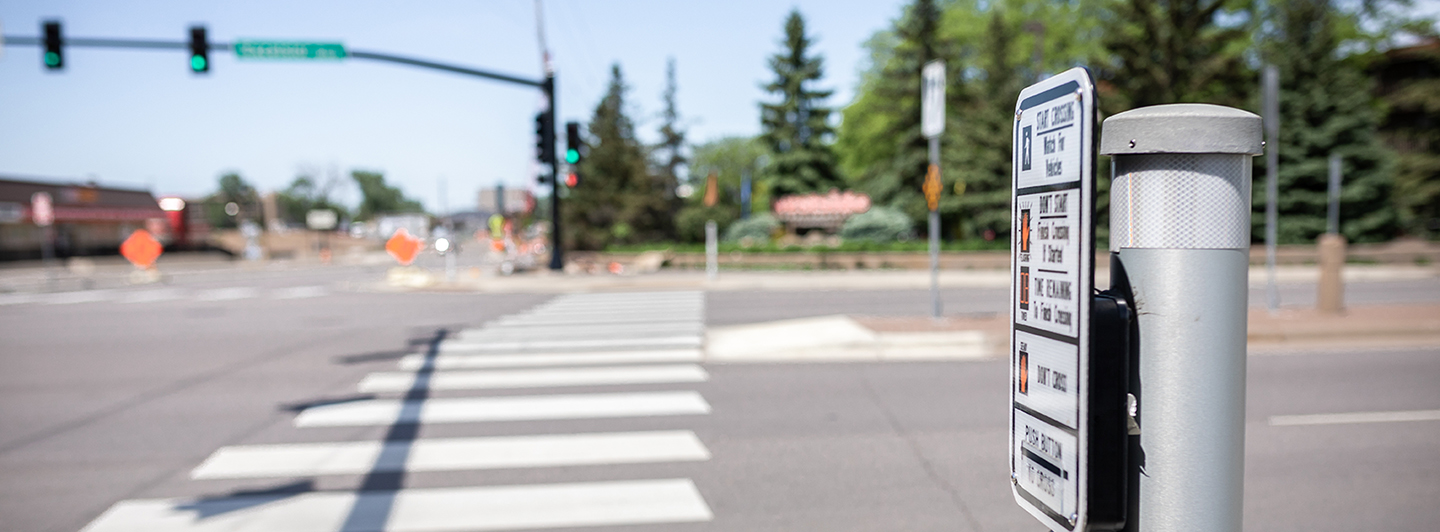 Close up of a crosswalk call button next to a sidewalk and street