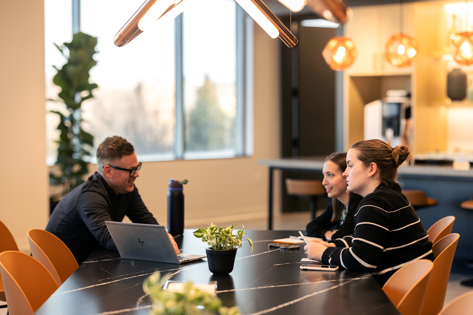 Three people working on a laptop at a table in an office setting