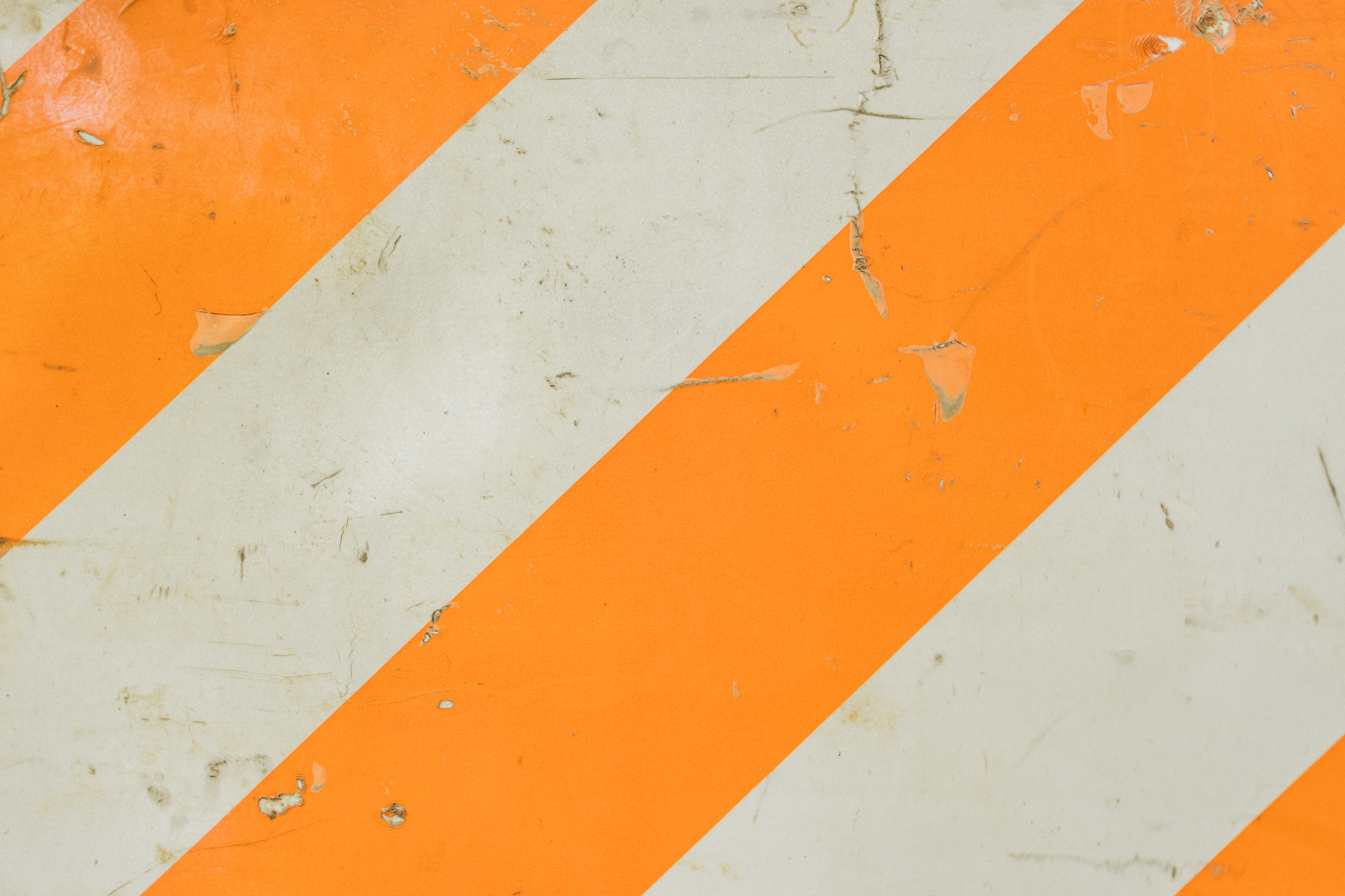 Surface with alternating diagonal orange and white stripes, worn and scratched, commonly used for safety or warning signs.