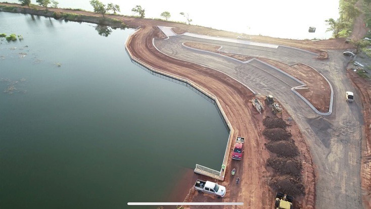 Aerial view of Altus Reservoir construction site featuring a newly built curved retaining wall along the water’s edge, with construction vehicles and equipment on adjacent paved and unpaved areas.