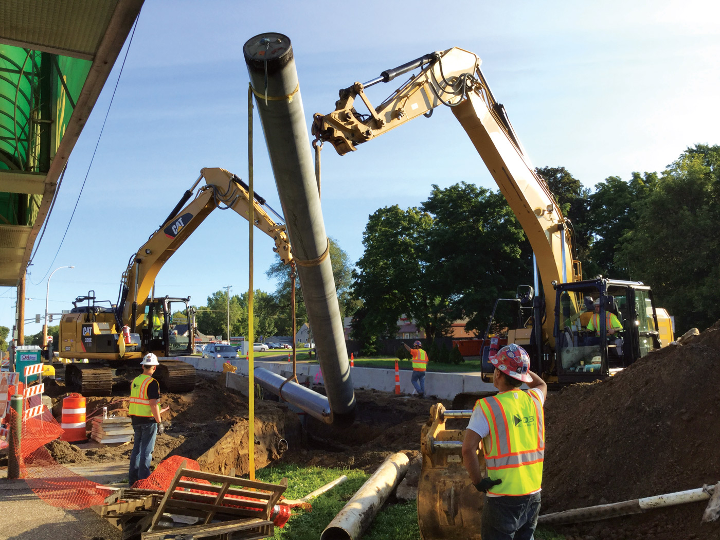 Workers and excavators positioning a long pipe section into an open trench during gas utility construction.