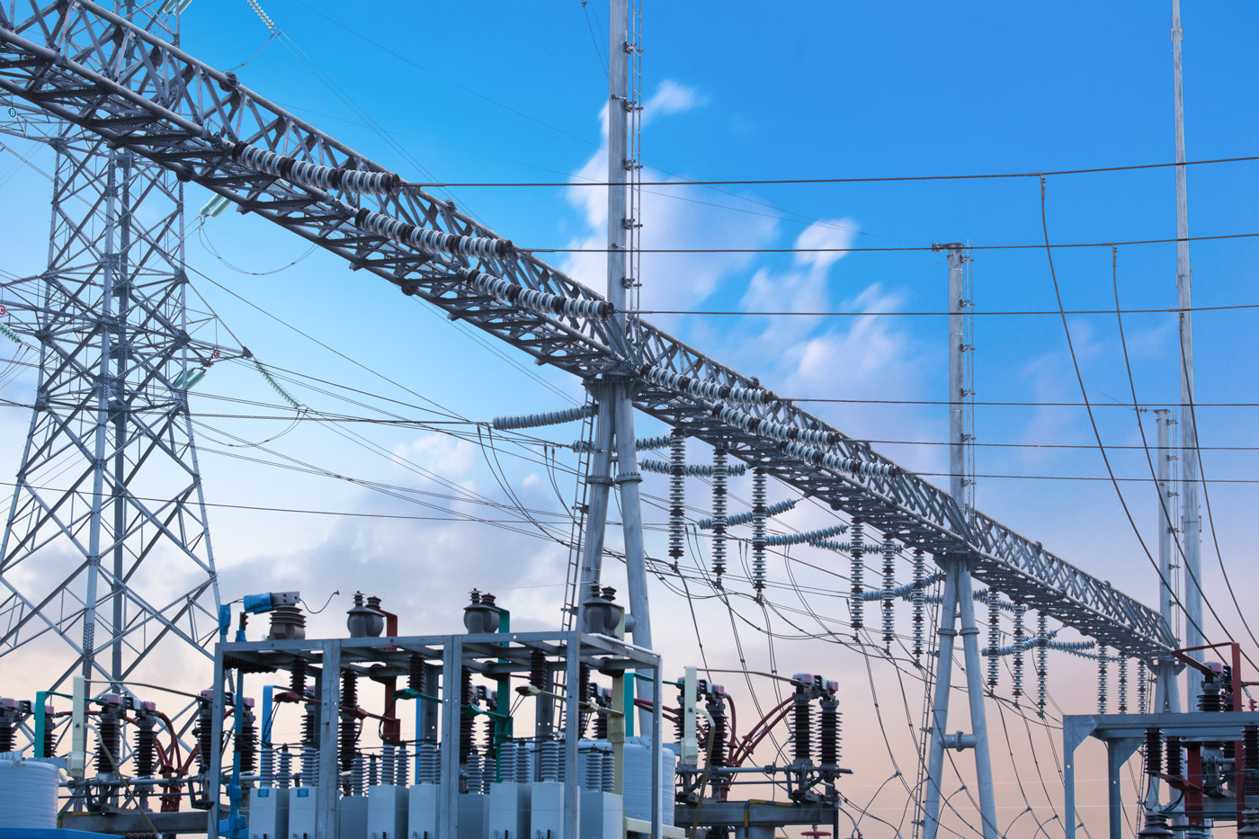 High‑voltage electrical substation with steel towers, conductors, and insulators against a blue sky, showing interconnected transmission equipment.