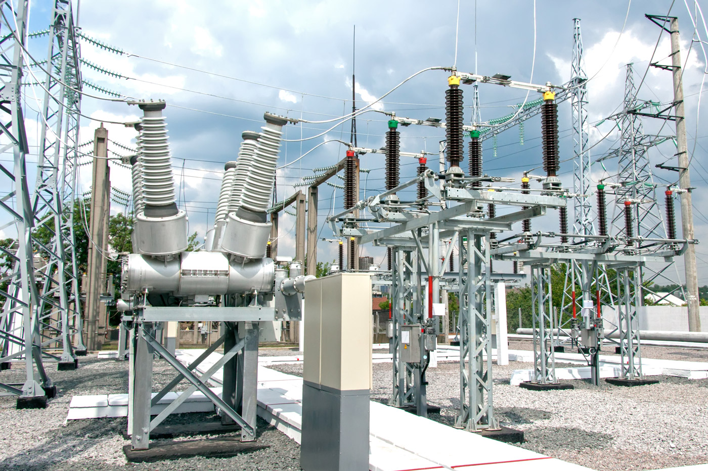 Outdoor electrical substation featuring high‑voltage circuit breakers, insulators, steel support structures, and interconnected overhead conductors. The equipment layout includes bushings, switchgear, and lattice towers, illustrating the components of a high‑voltage transmission and distribution system.