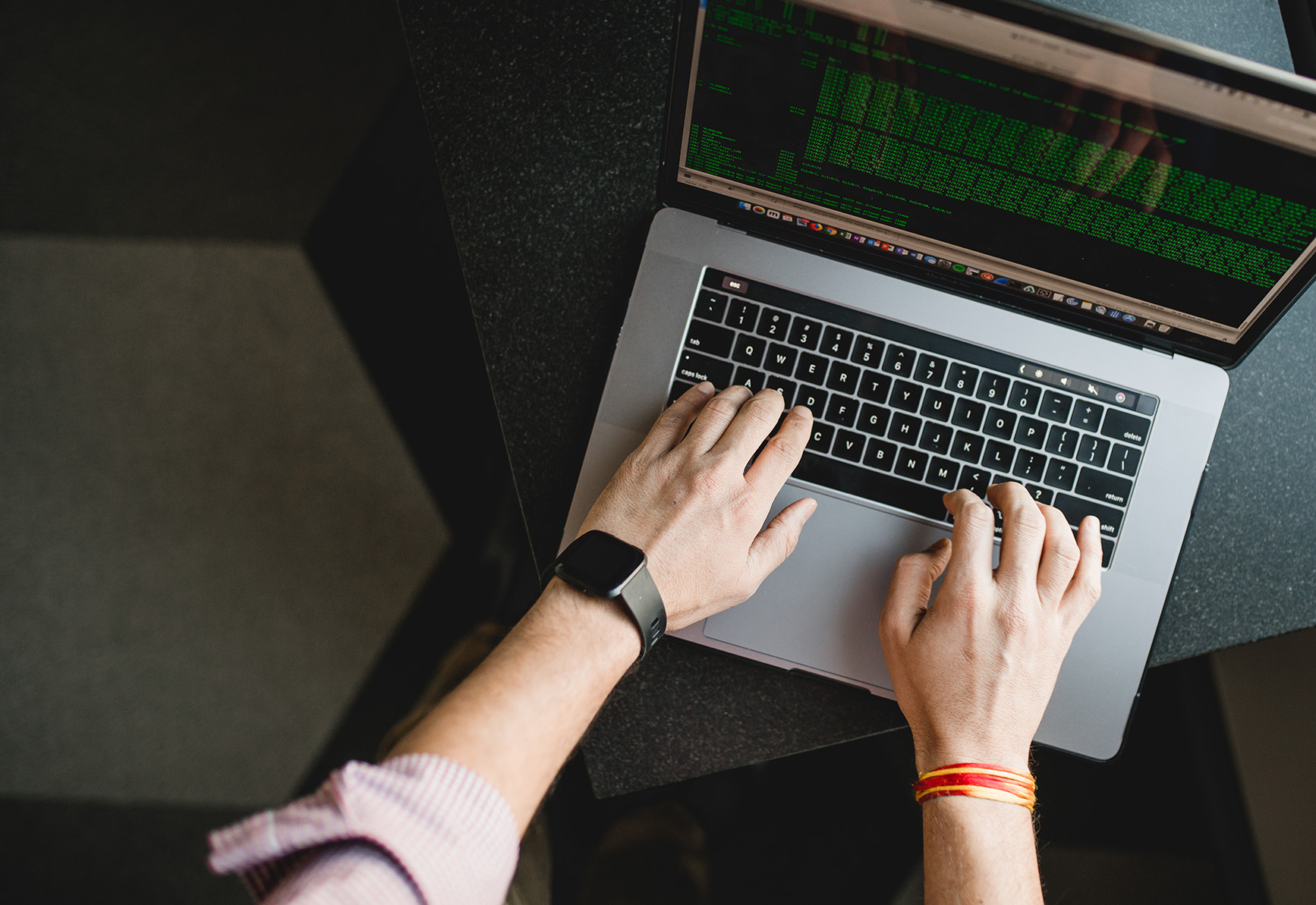 Hands typing on a laptop keyboard, viewed from above, with green lines of code displayed on the screen.