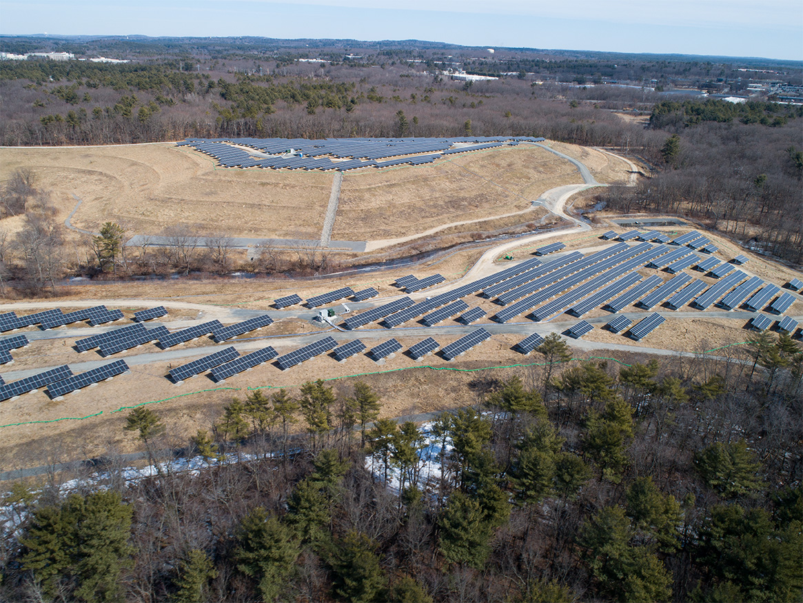 Wide aerial view of the Tewksbury solar project on a capped landfill, illustrating panel layout, site grading, and surrounding landscape.