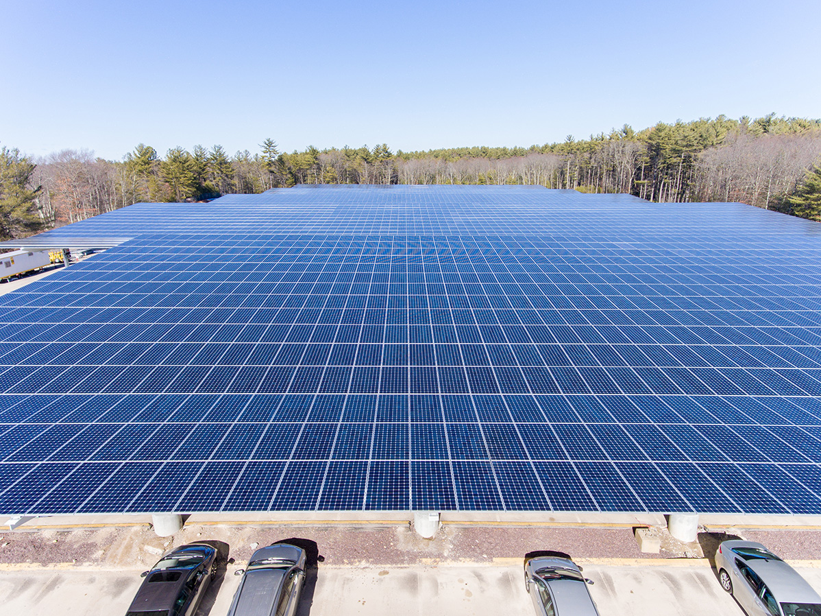 Front view across solar carport canopies at Stonehill College, illustrating the elevated photovoltaic panel layout above parked vehicles.