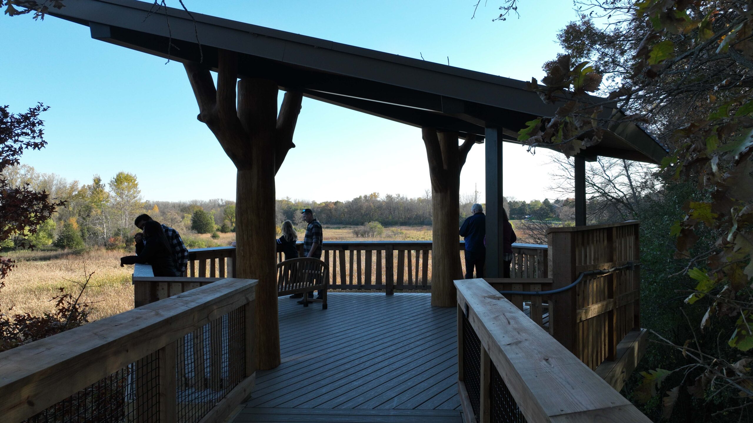 Covered overlook platform with wood railings, where visitors observe an open prairie and wetland landscape below.