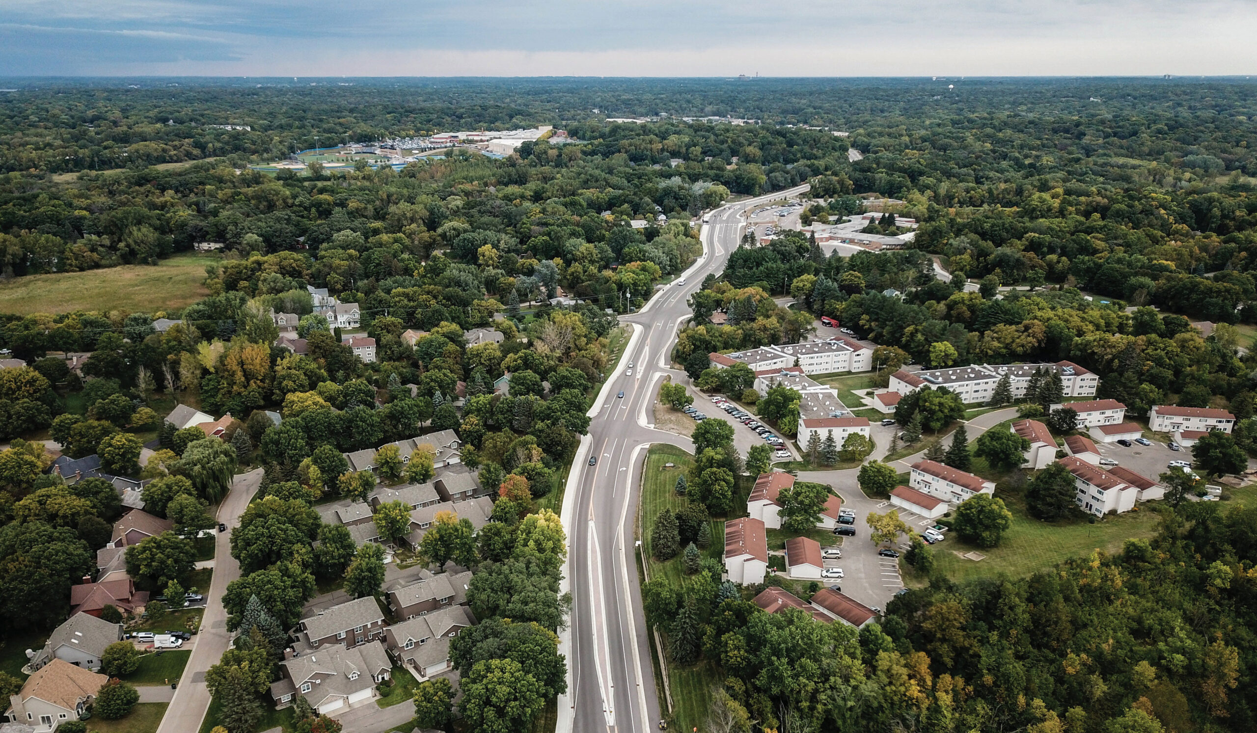 Aerial view of a suburban neighborhood with tree-lined streets, residential homes, and a multi-lane roadway connecting the community.