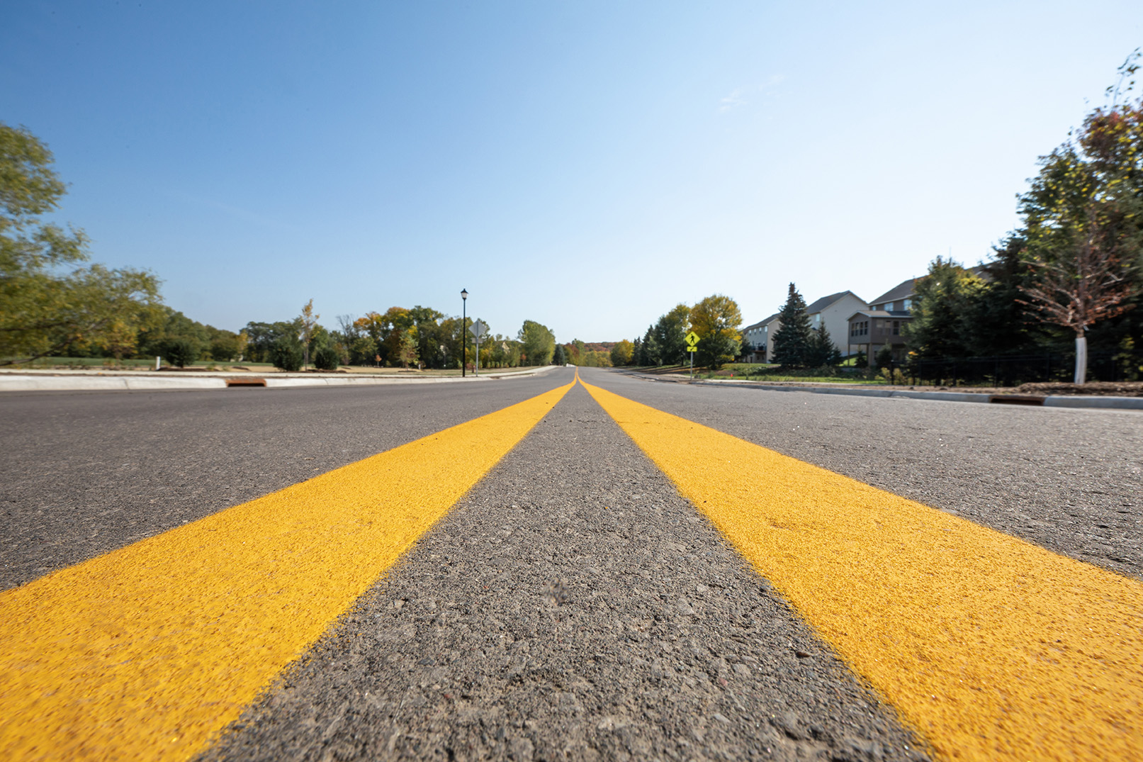 Low-angle view of a paved roadway with double yellow centerlines stretching into the distance in a suburban area.