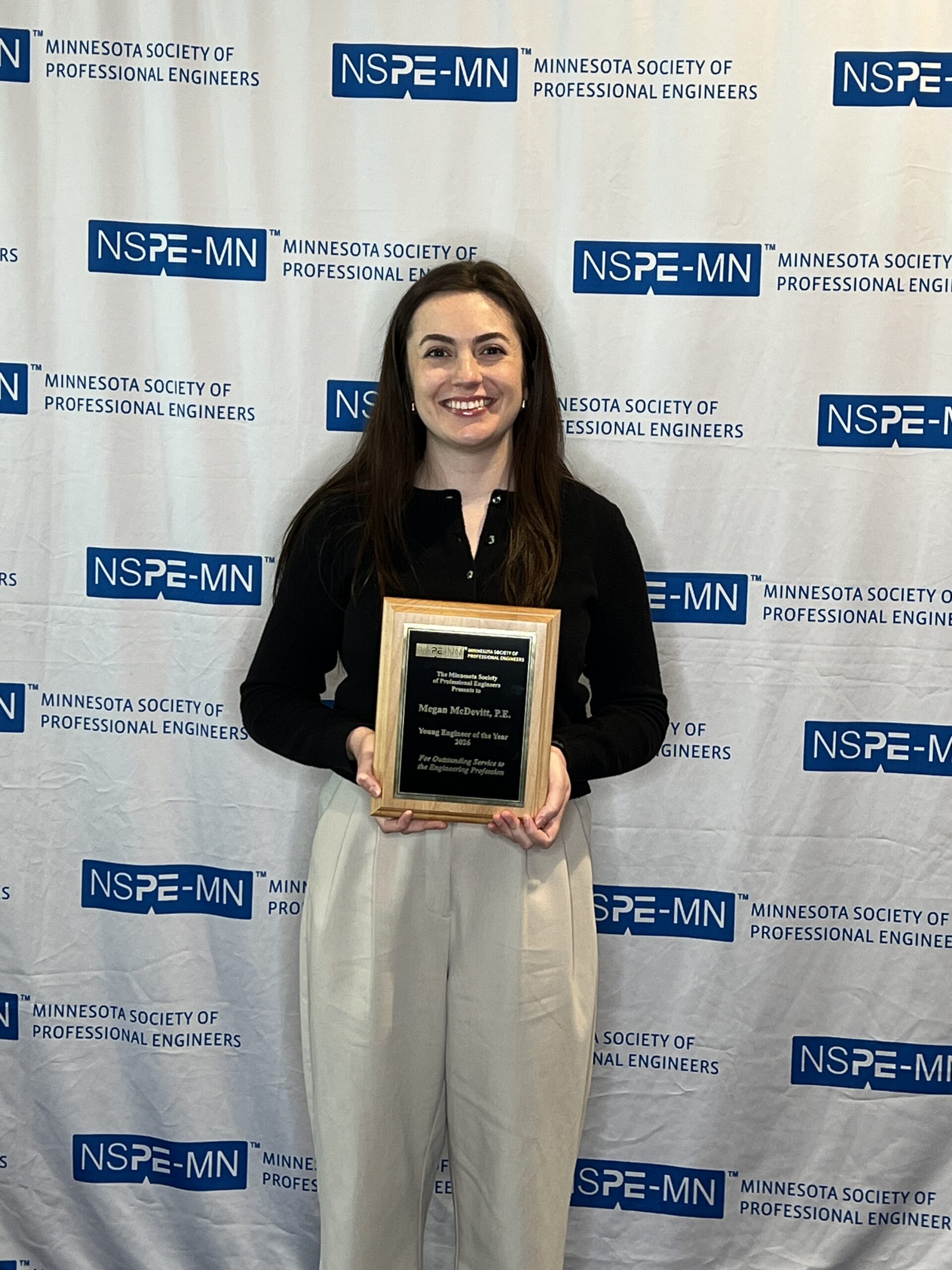 Megan McDevitt standing in front of an NSPE‑MN backdrop holding an award plaque.
