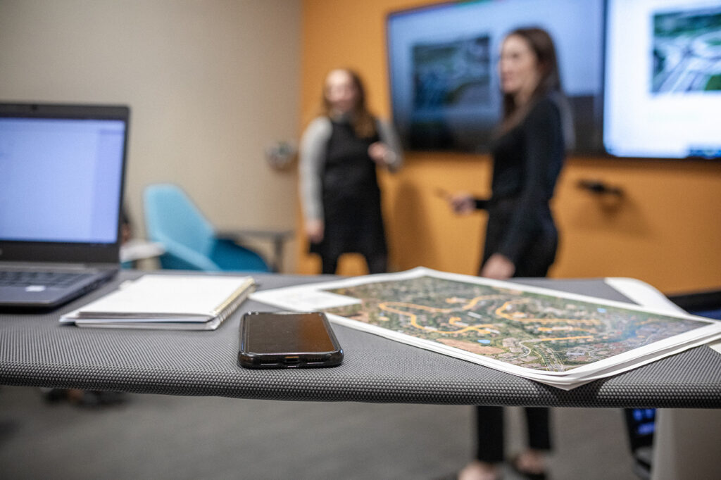 Maps, project documents, and meeting materials are displayed on a conference room table during a collaborative planning and strategy session.