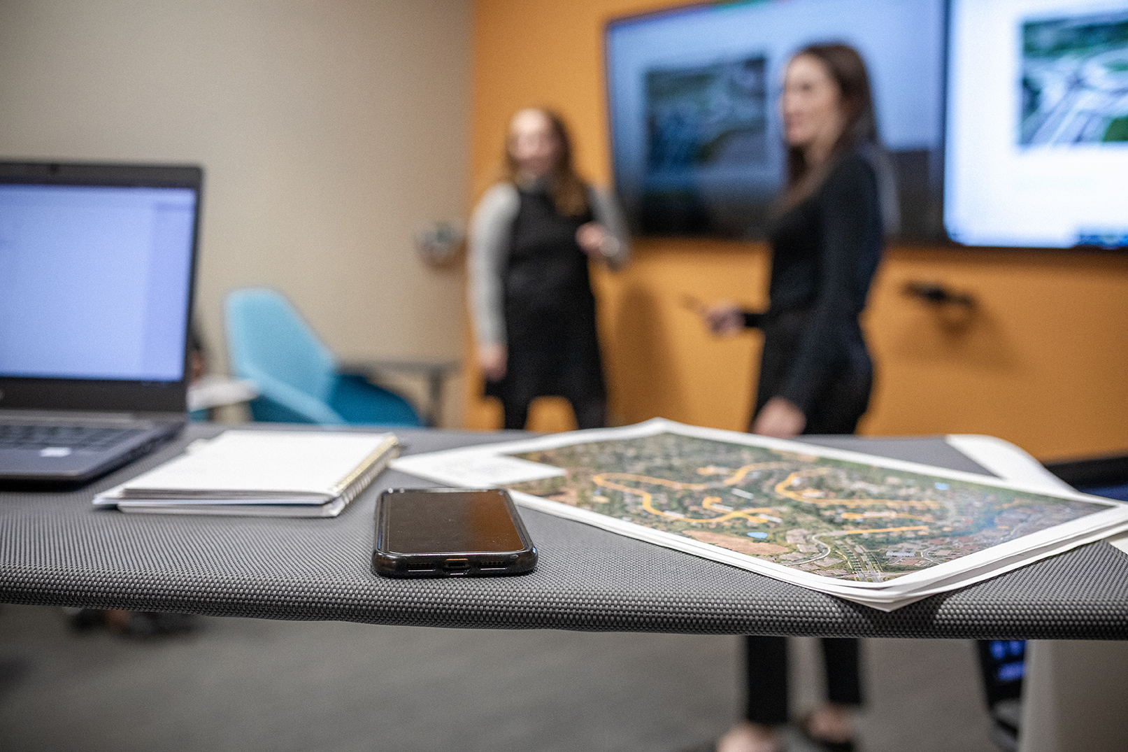 Maps, project documents, and meeting materials are displayed on a conference room table during a collaborative planning and strategy session.