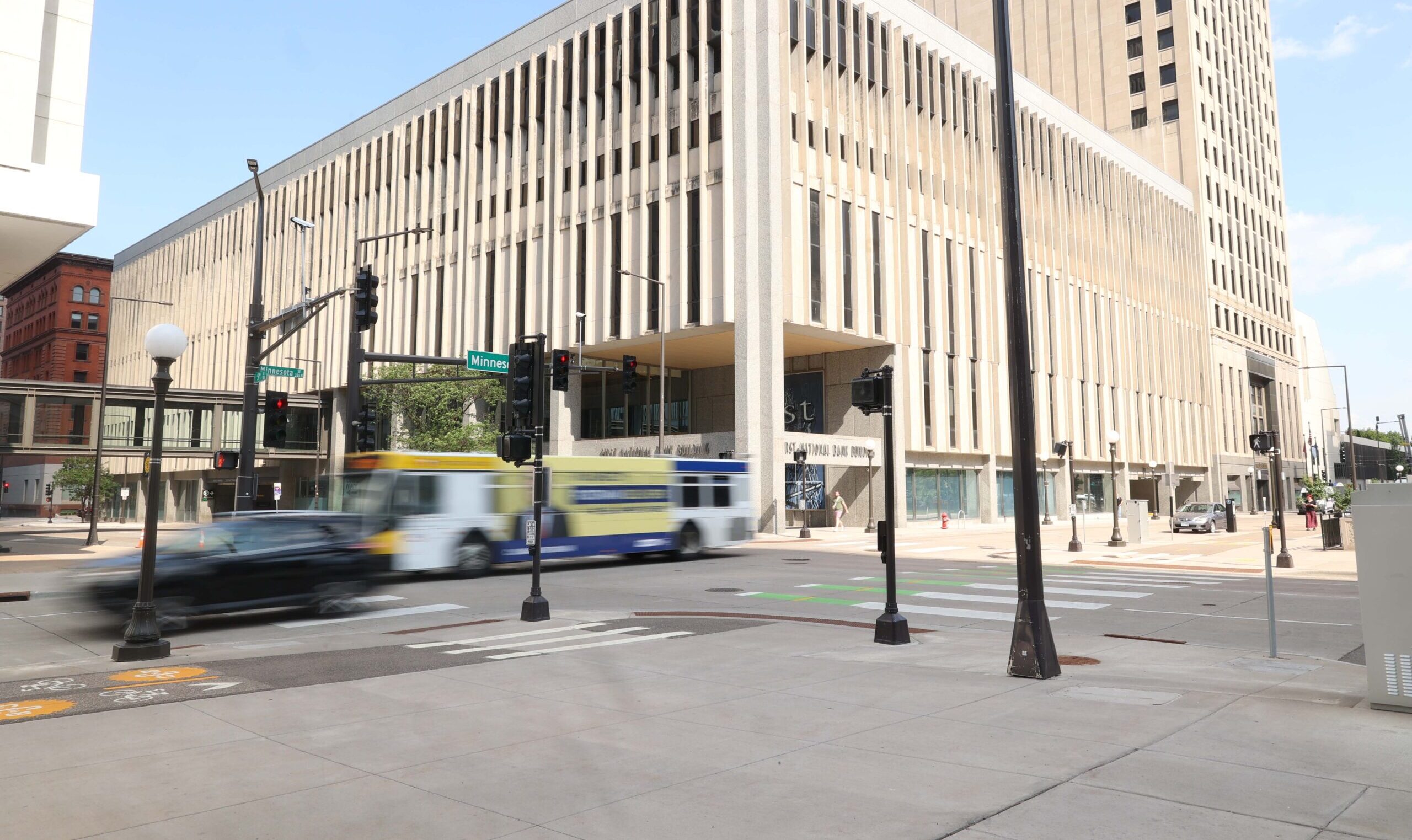 Bus and vehicle traveling through a signalized downtown intersection with marked crosswalks and bike lanes.