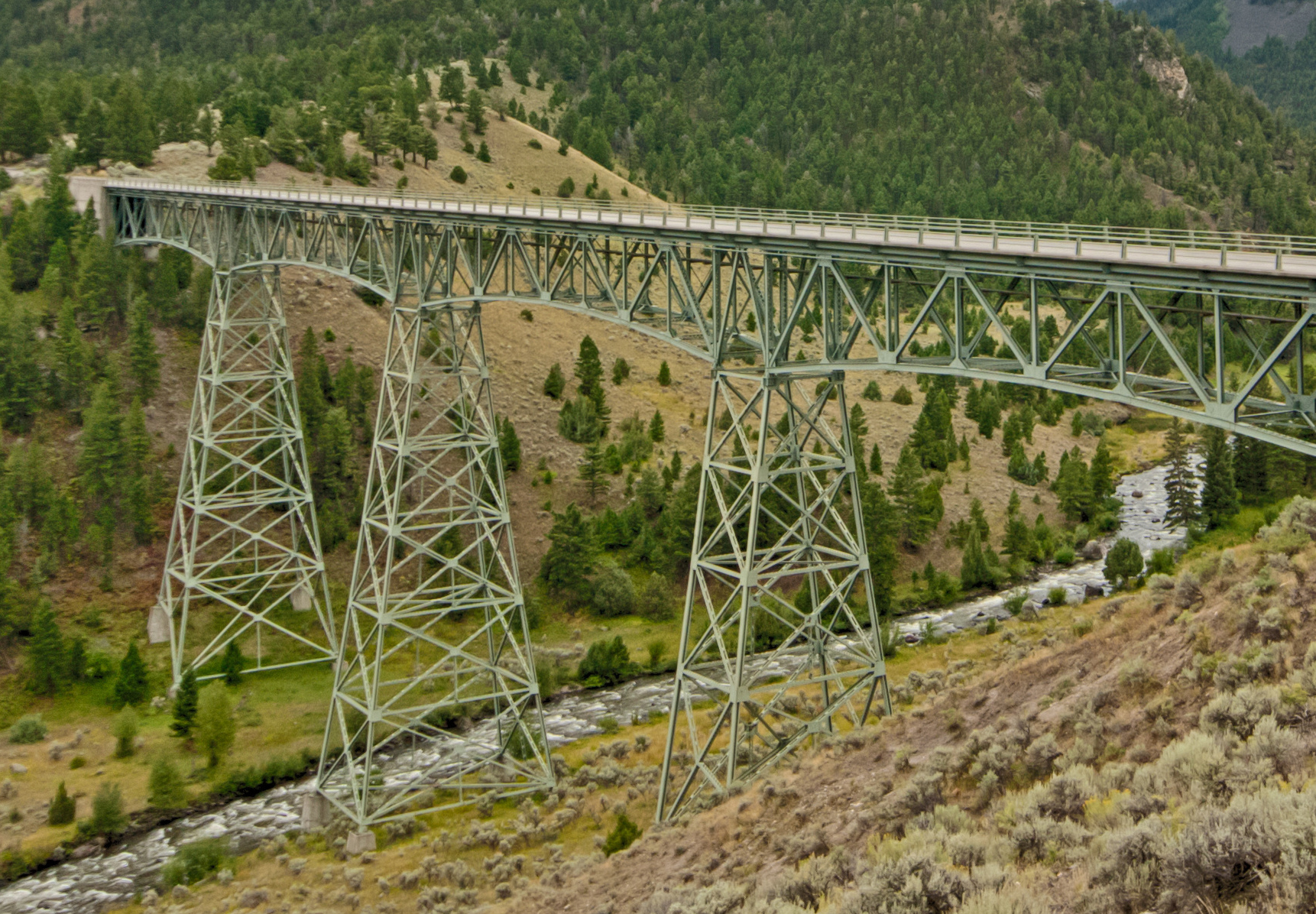 Steel truss bridge spanning a river through a forested mountain landscape.