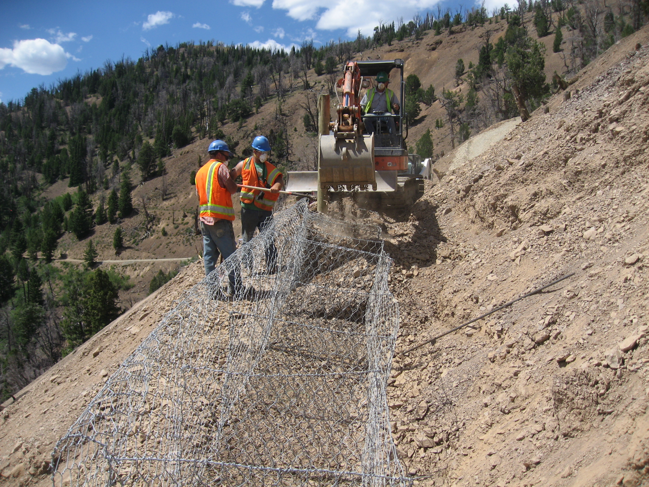 Historic Bayhorse Mine structures on a hillside with wooden fencing, native vegetation, and mountain scenery.